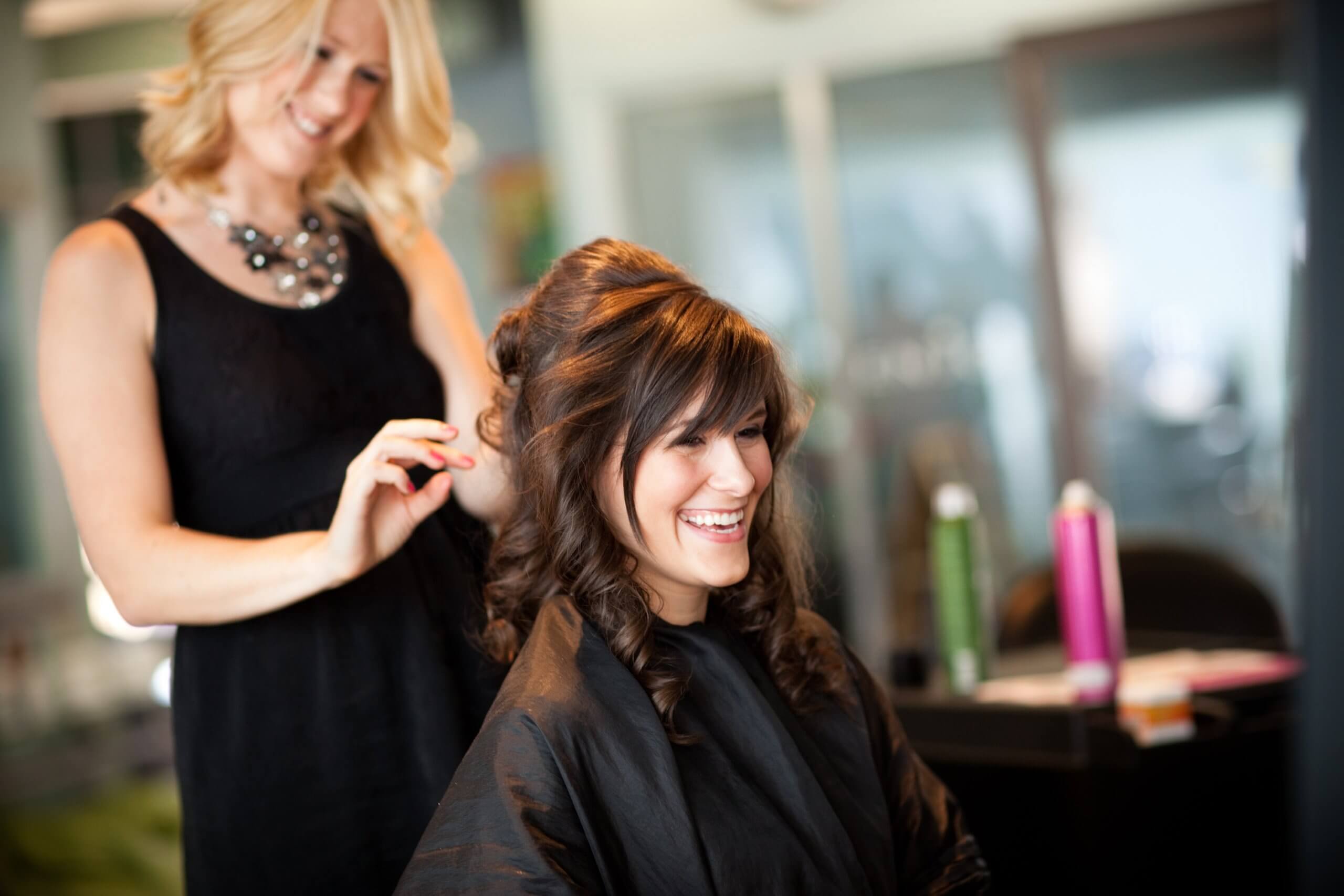 A hairstylist smiles as she styles a happy client's hair in a modern salon, capturing the thriving atmosphere where excellent service leads to increased revenue.