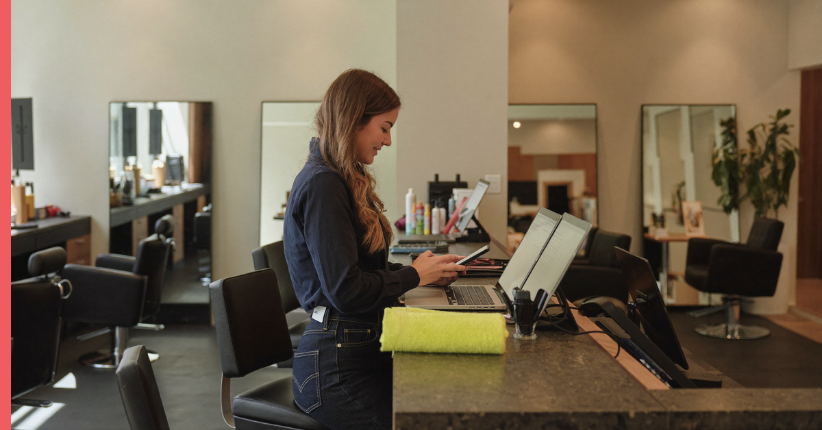 Salon owner sending a salon SMS marketing campaign from the front desk of a quiet salon